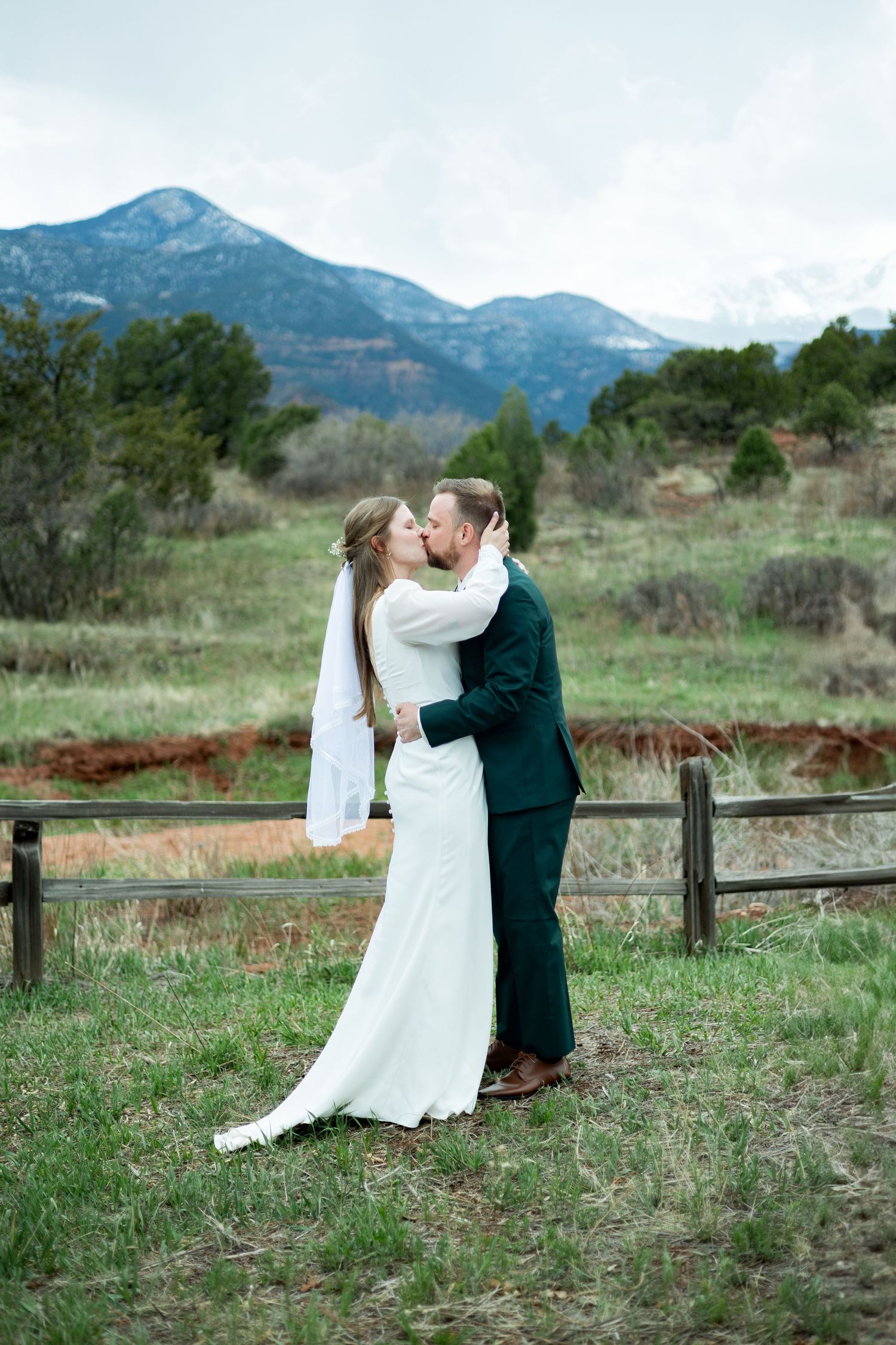 A romantic wedding photo with mountains and rustic fence in Colorado countryside.