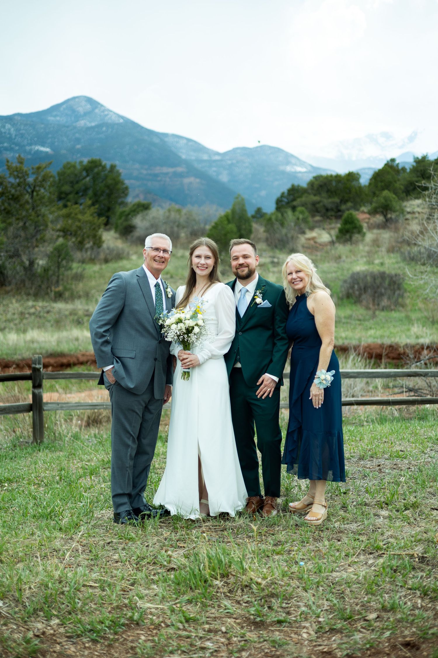 Group poses for outdoor wedding photo with mountain backdrop in Colorado, showcasing elegant attire and natural scenery.