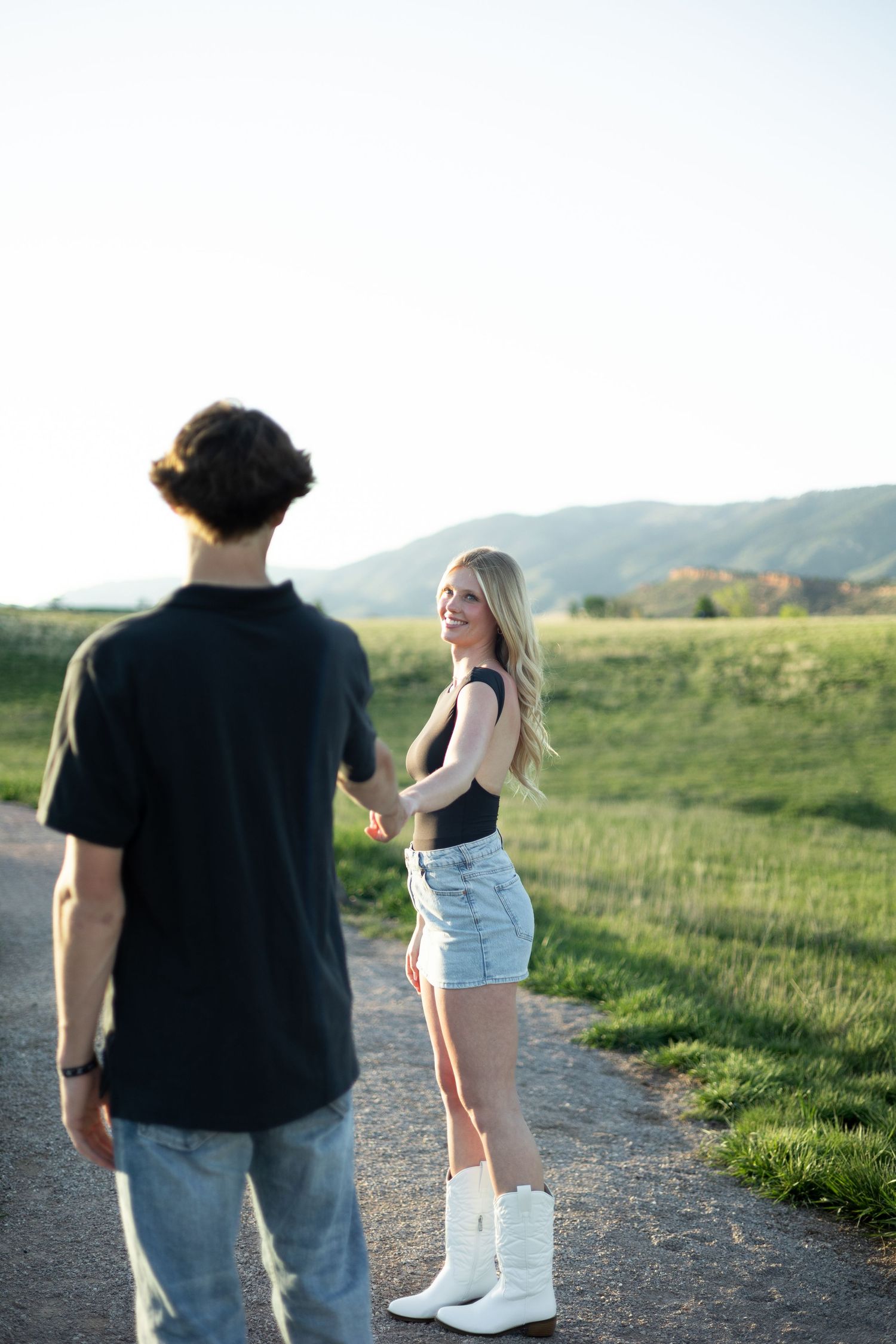 A couple walking along a scenic dirt trail through green hills during a sunny evening.