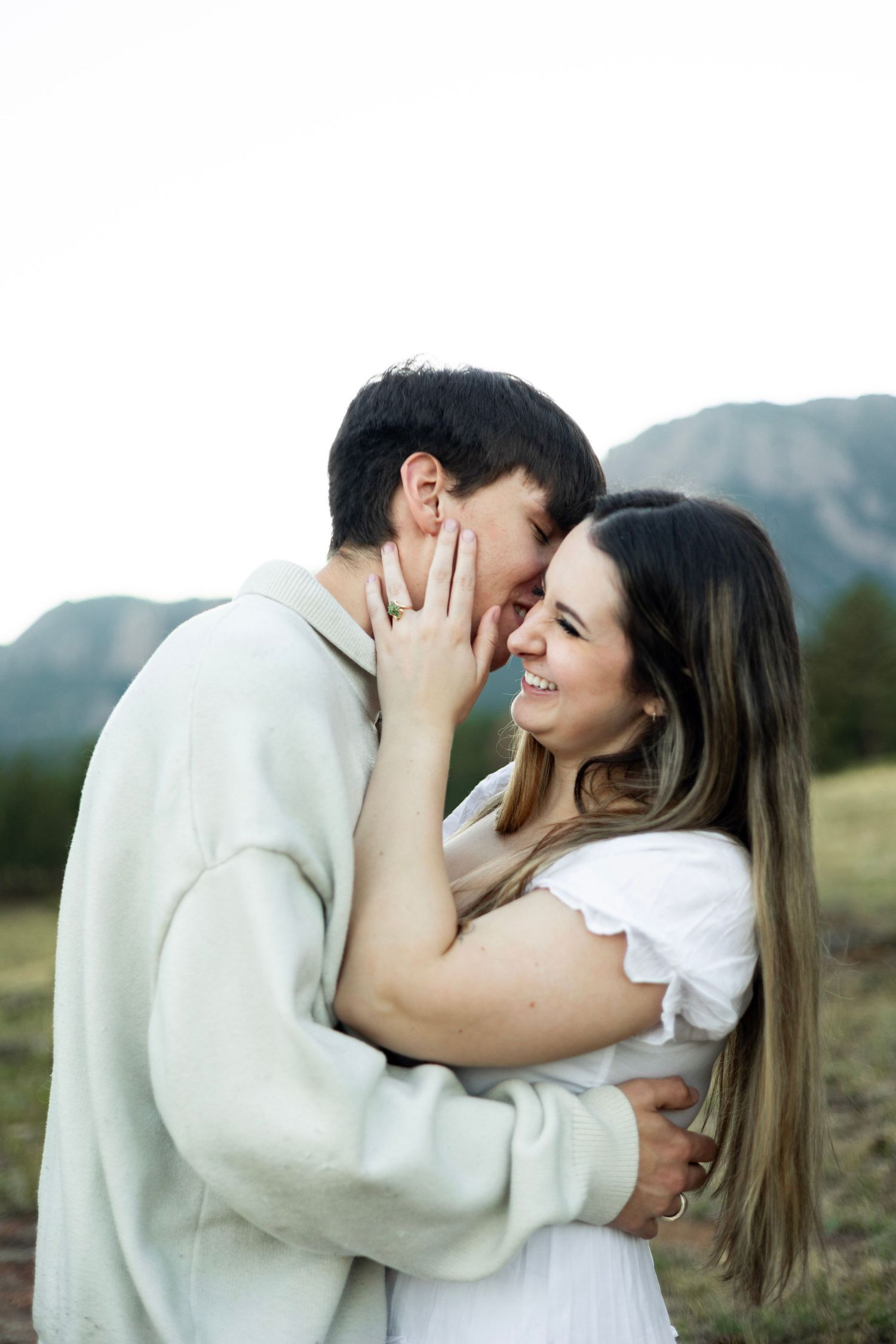 Two people share an intimate moment while embracing outdoors in white clothing.