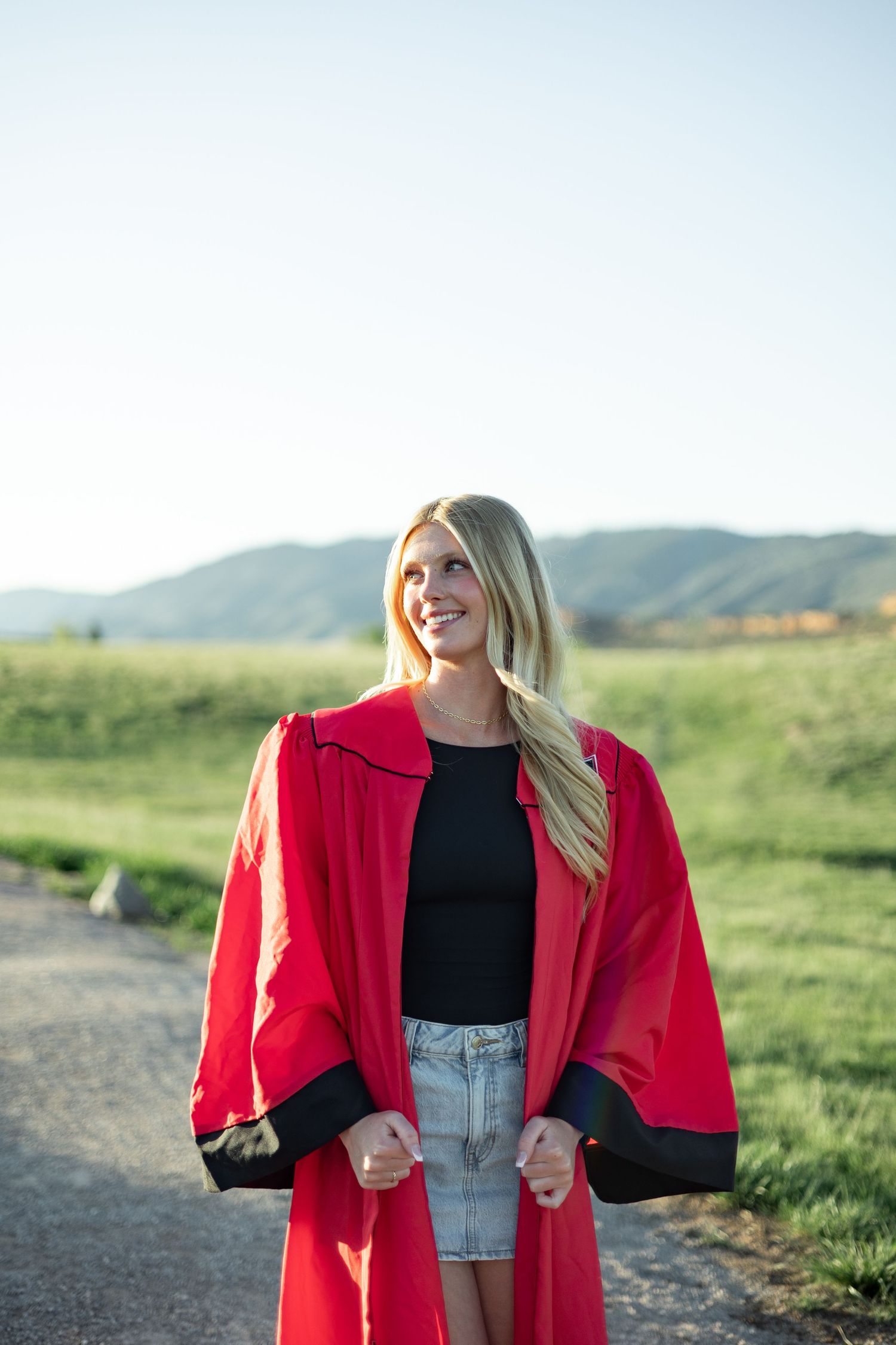 A bright red coat stands out against rolling green hills and a dirt path on a sunny afternoon.