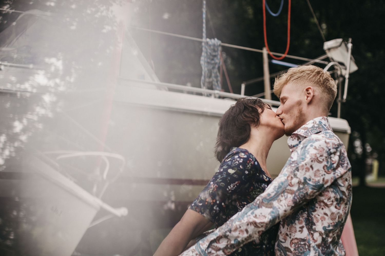 A romantic couple share an intimate kiss outdoors in moody lighting with a dreamy double exposure effect.