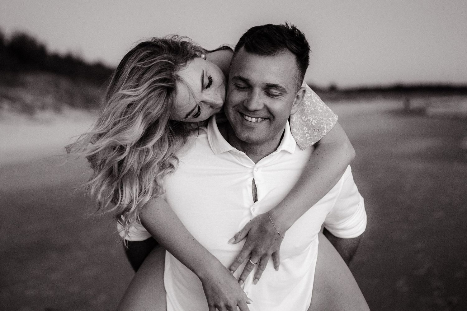 Black and white photo of a romantic couple embracing on a beach at sunset.