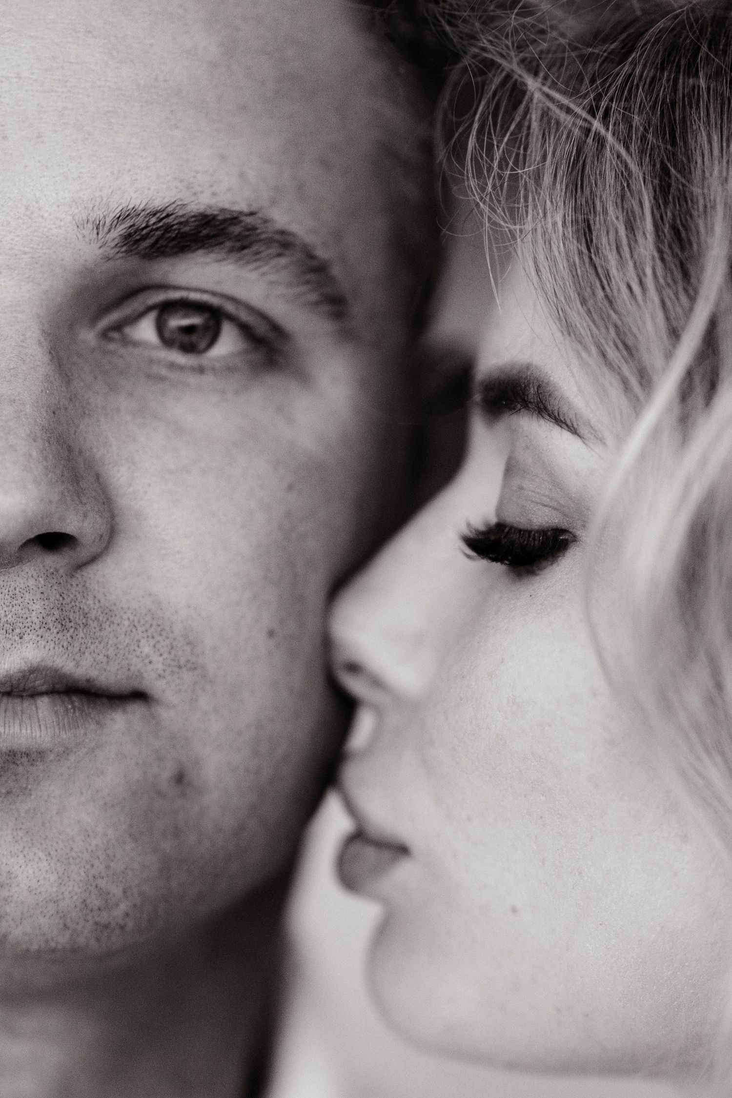 Black and white close up intimate portrait showing half faces in profile with soft lighting and romantic mood.