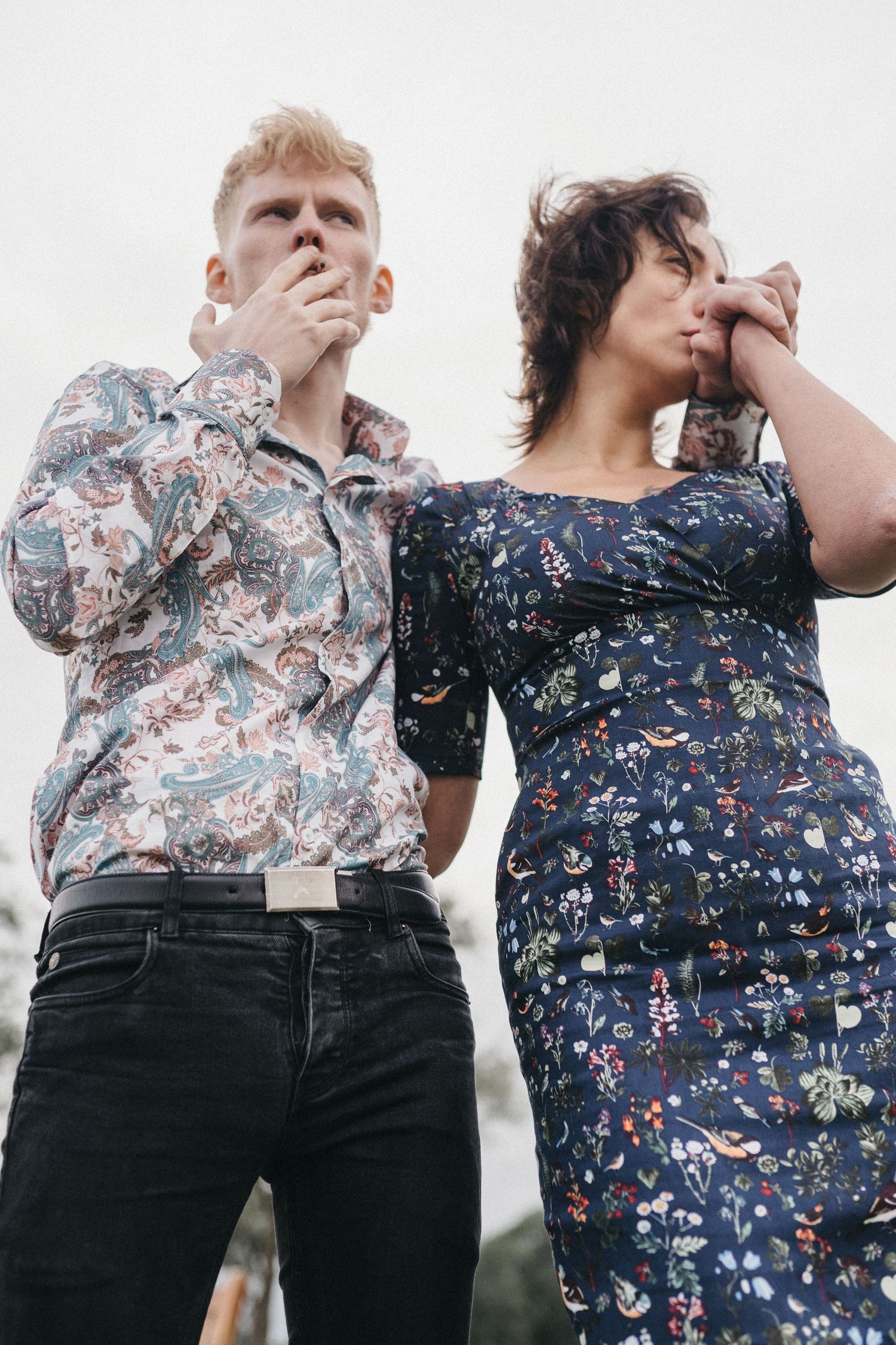 Two people in patterned clothing posing dramatically against a light background with hands near their faces.