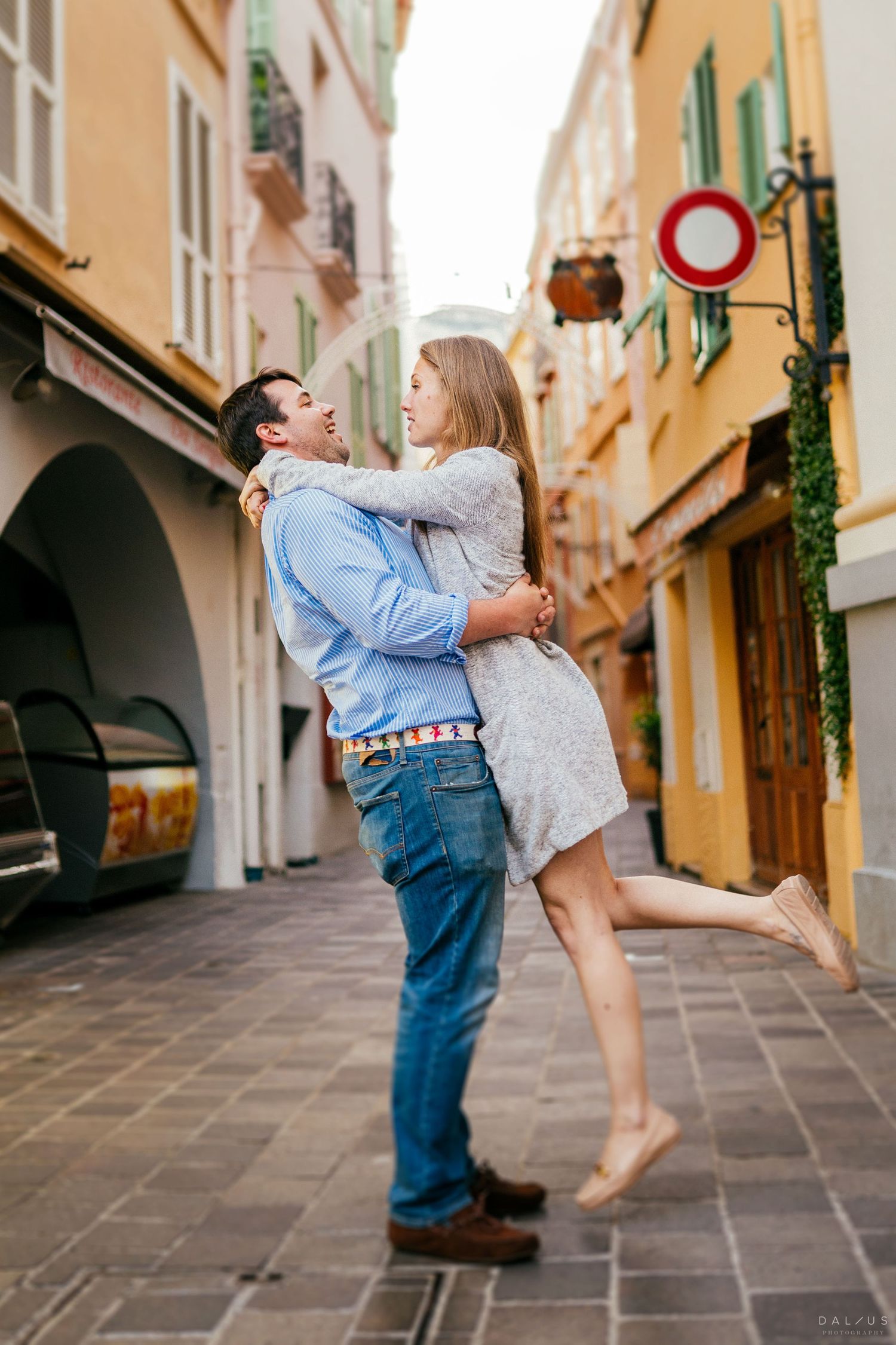 A couple shares a romantic embrace on a charming European cobblestone street with colorful buildings in the background.