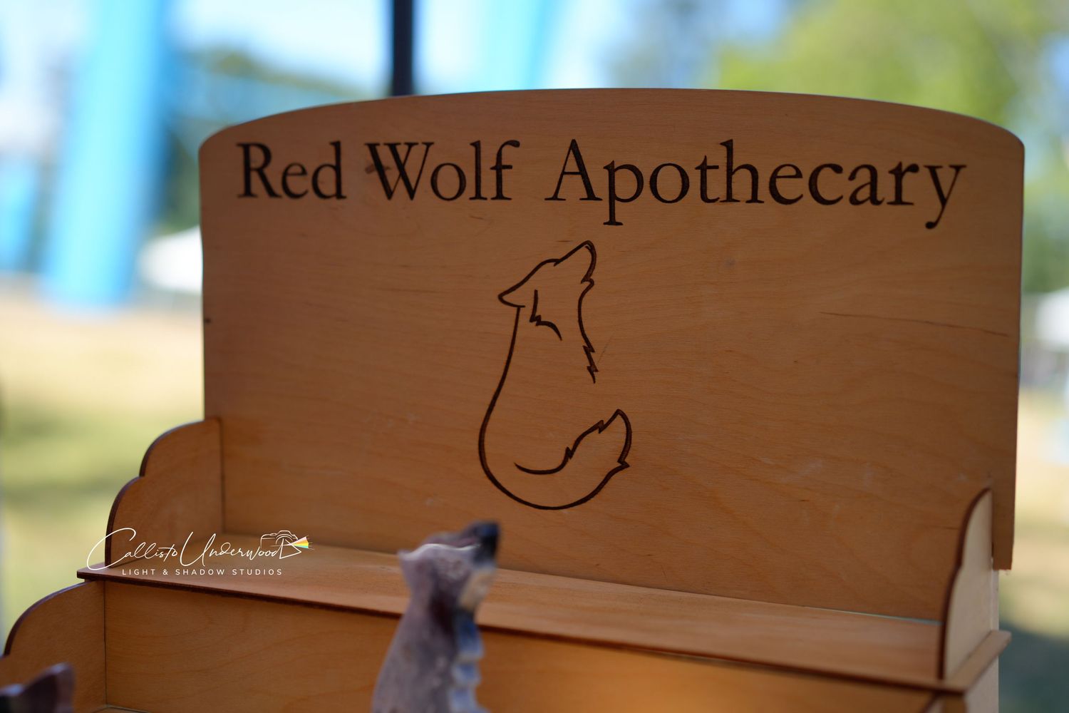 Wooden Red Wolf Apothecary sign with a laser-engraved howling wolf design on a vendor display at an outdoor market.