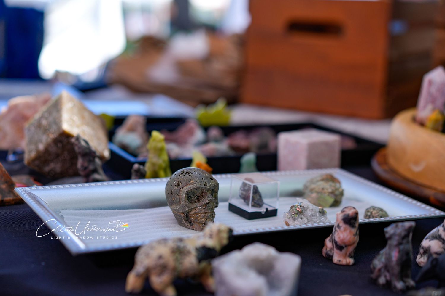 Handmade skull carving and assorted polished crystals and figurines displayed on a white tray at an outdoor craft market.