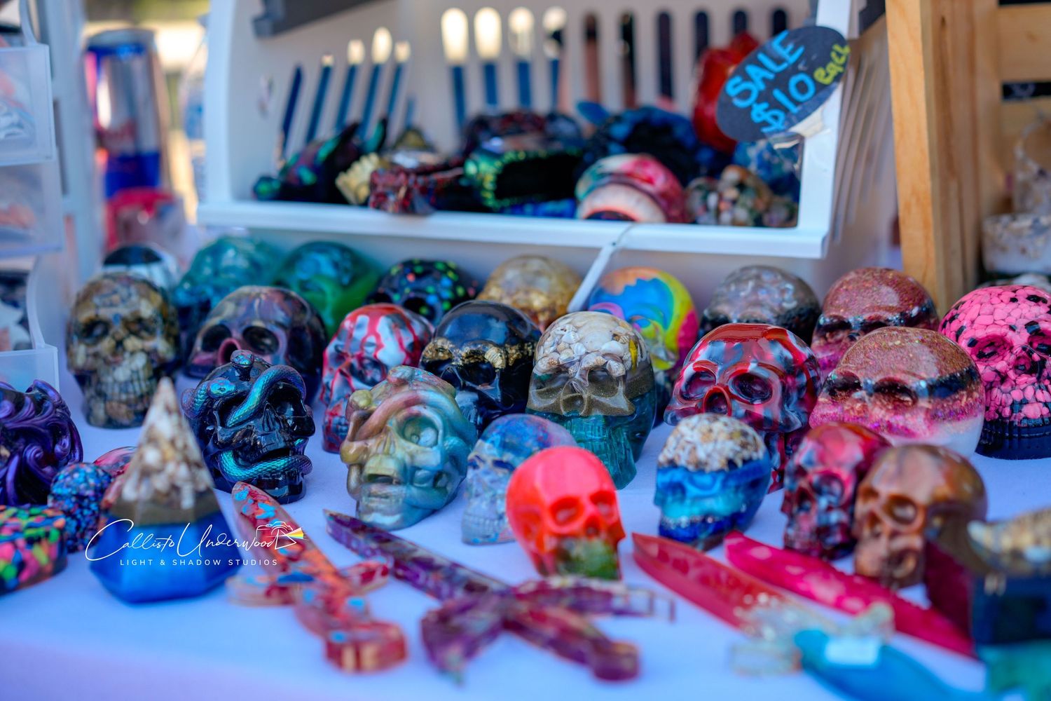 Colorful painted sugar skulls and decorative crosses displayed on a table at an outdoor craft market vendor booth.