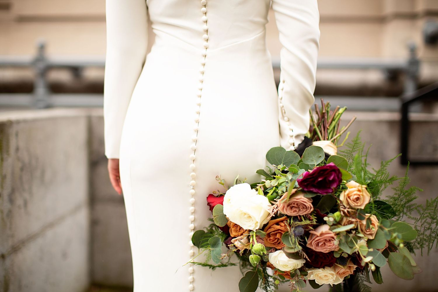 Elegant white wedding dress with button details and autumn-colored bouquet.