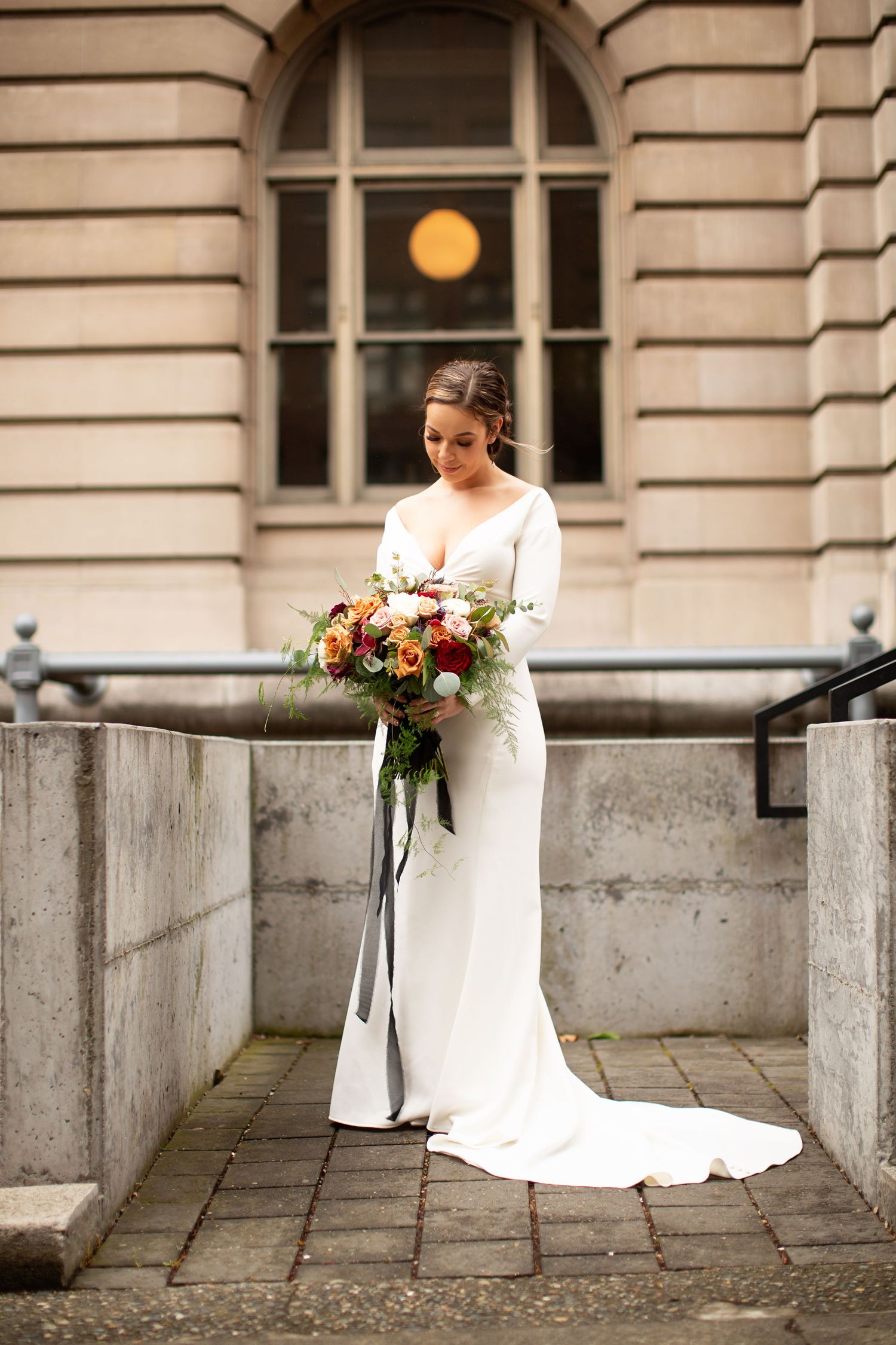 Person in white wedding dress holding colorful bouquet against classic stone architecture.