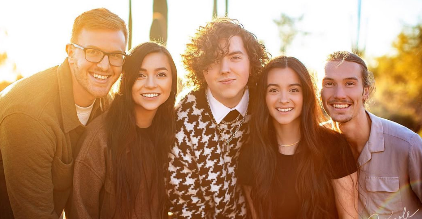 Friends posing together in casual attire with sunset backlighting.
