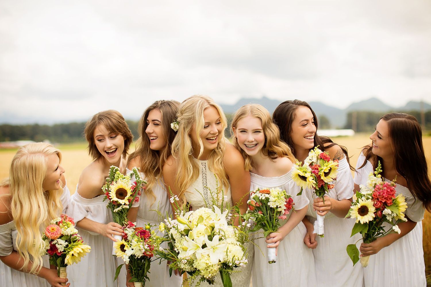 Bridal party holds bright yellow sunflower bouquets in a summer field.