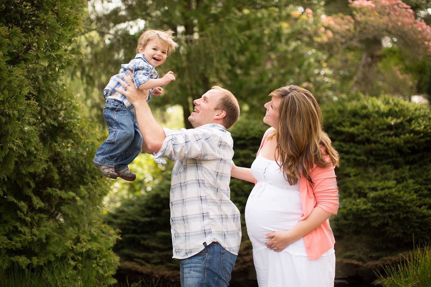 Joyful family moment in garden with toddler being lifted high.