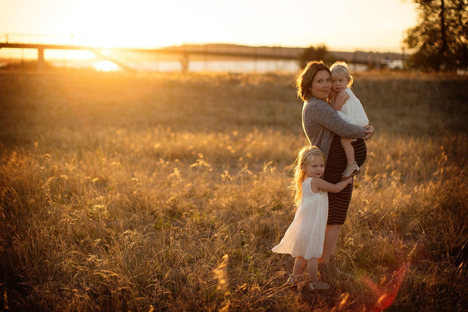 Romantic sunset portrait in golden field with bridge in background.