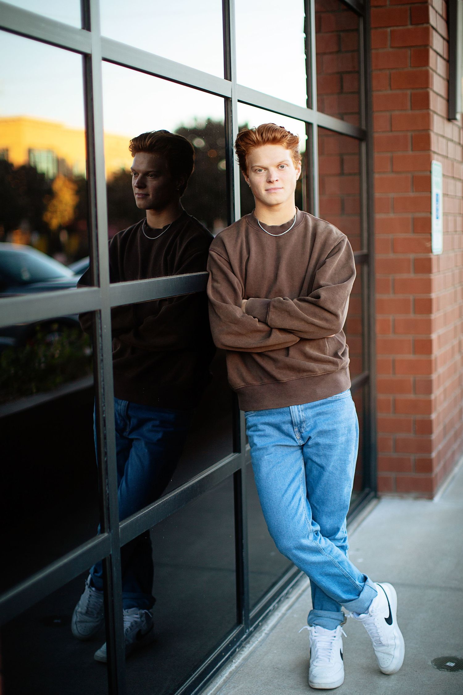 Urban portrait session against brick building with reflective windows.