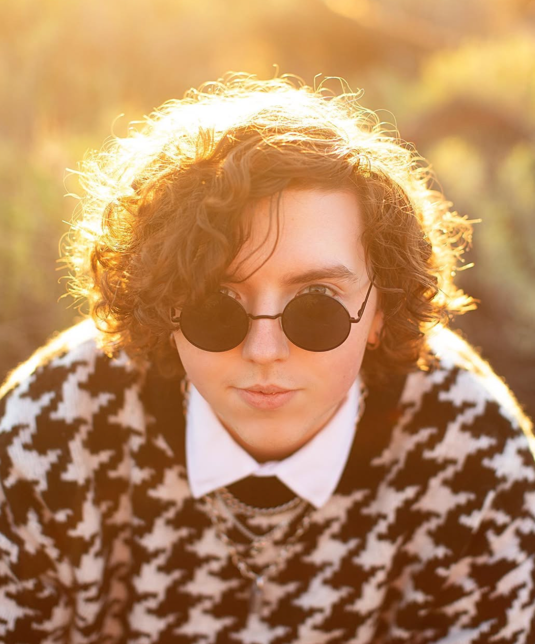Close up portrait of someone wearing sunglasses and a houndstooth pattern coat in warm sunlight.
