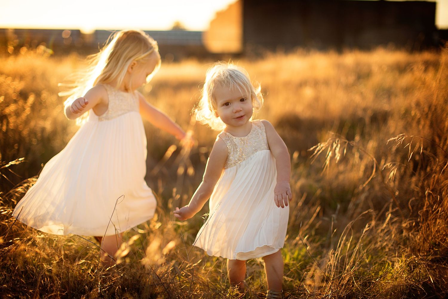 White flowing dresses captured in golden sunlight on grassy hillside.