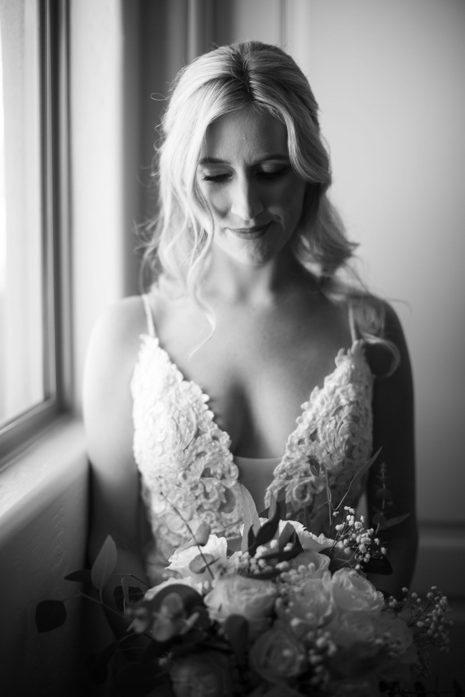 Black and white portraits of bride holding bouquet near window in elegant lace gown.