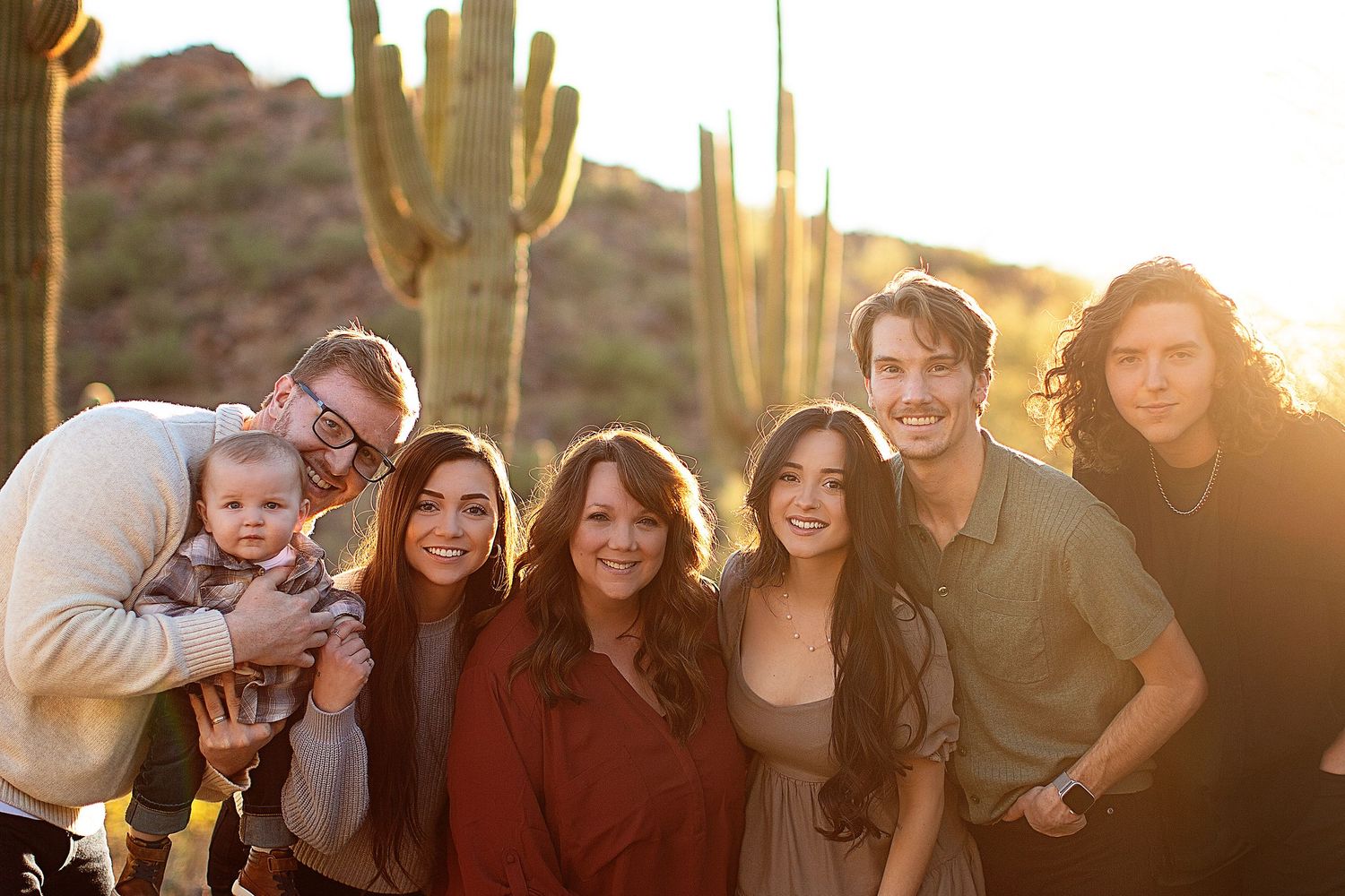 A group poses together outdoors with desert cacti and golden sunset lighting in the background.