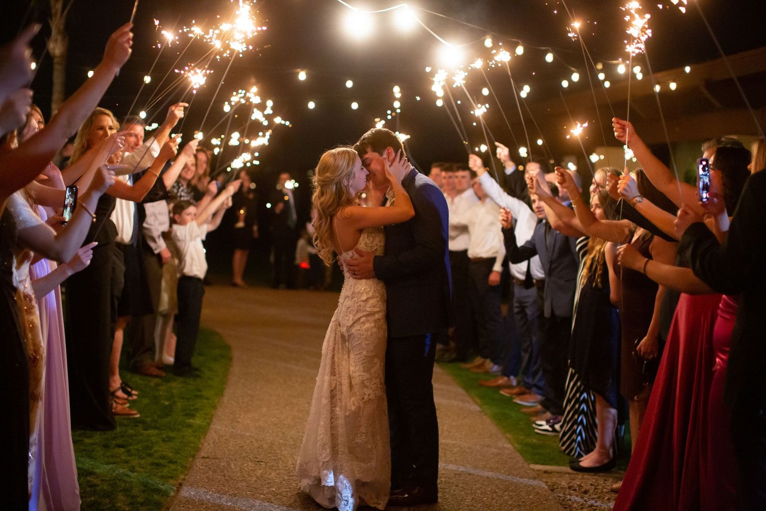 Wedding guests hold sparklers creating magical nighttime exit tunnel.