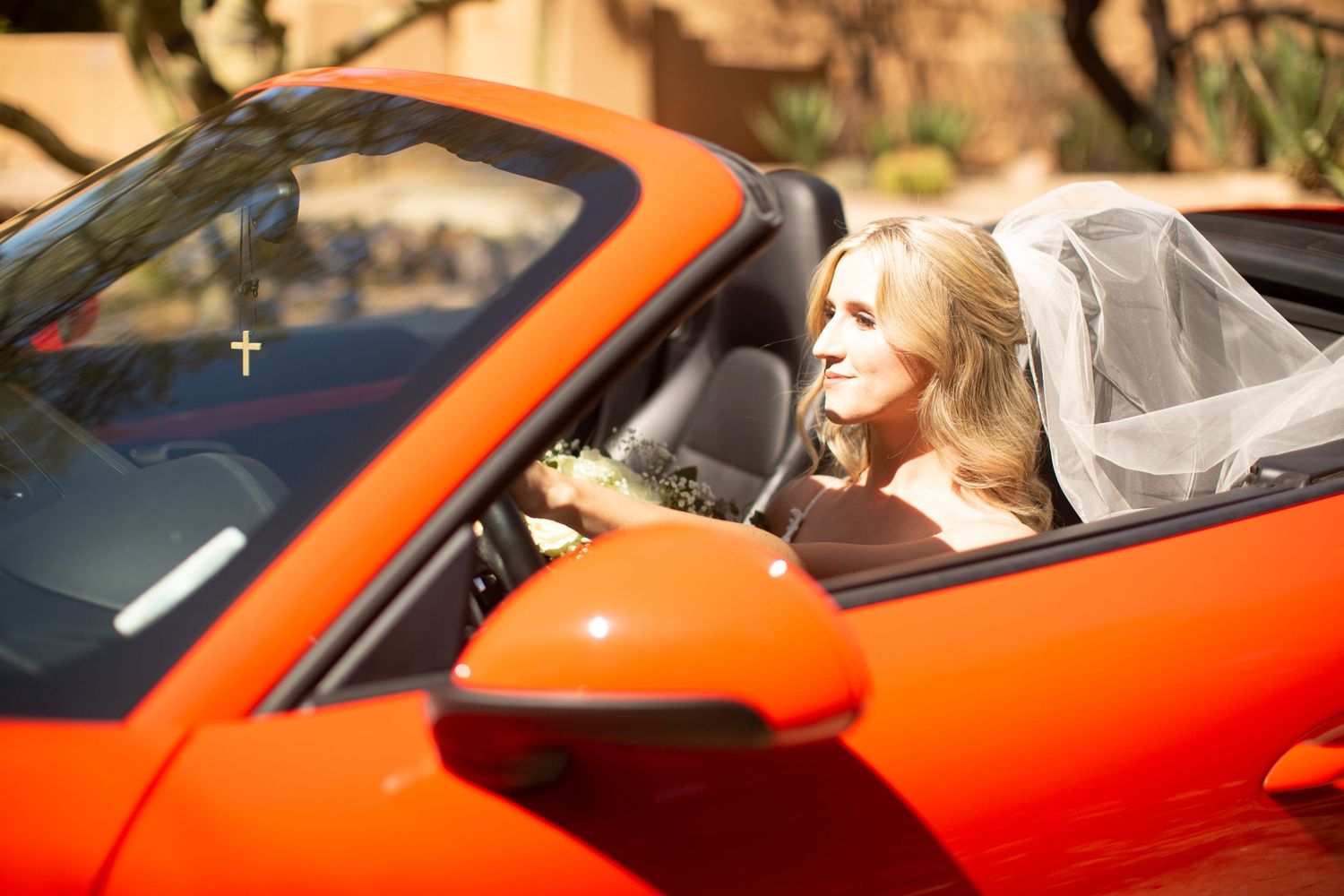 Wedding couple rides in bright orange sports car during celebration.
