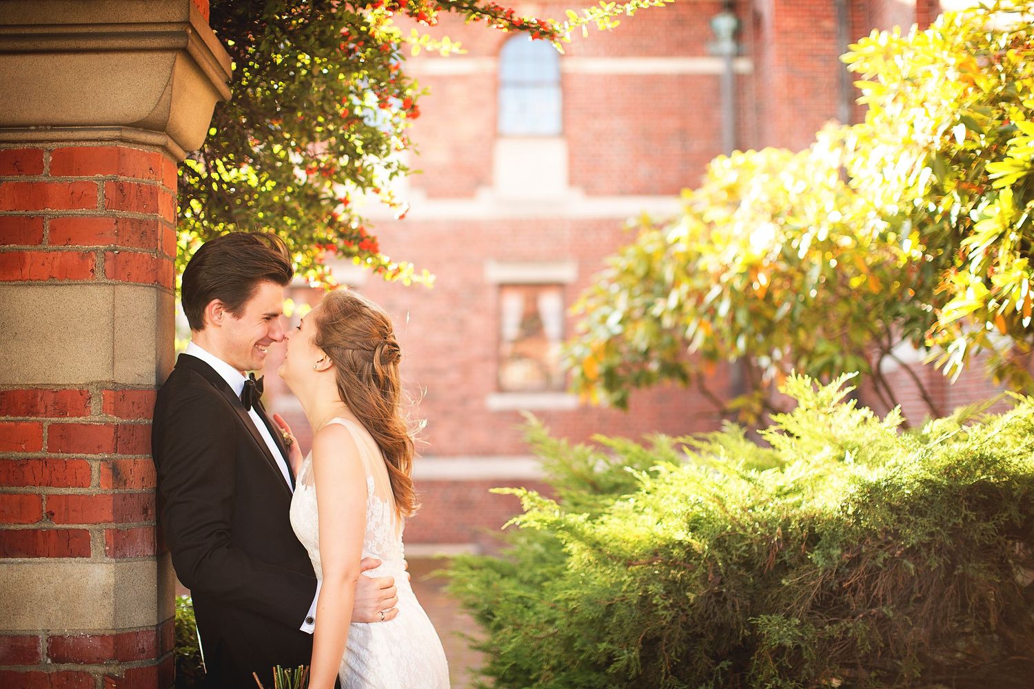 Sunlit wedding portraits with autumn foliage and brick architecture.