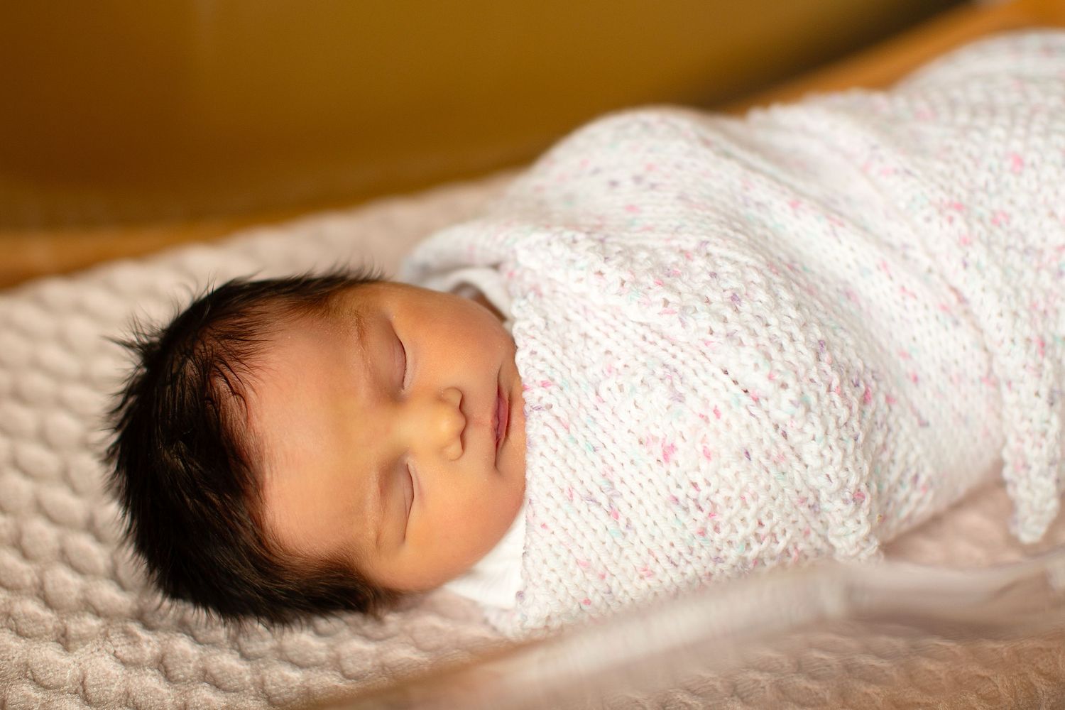 A sleeping baby wrapped in soft white blankets on a textured surface.