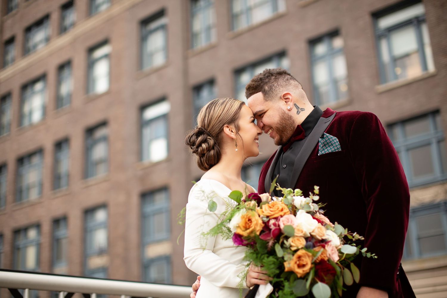 A couple shares an intimate moment against an urban brick building backdrop.