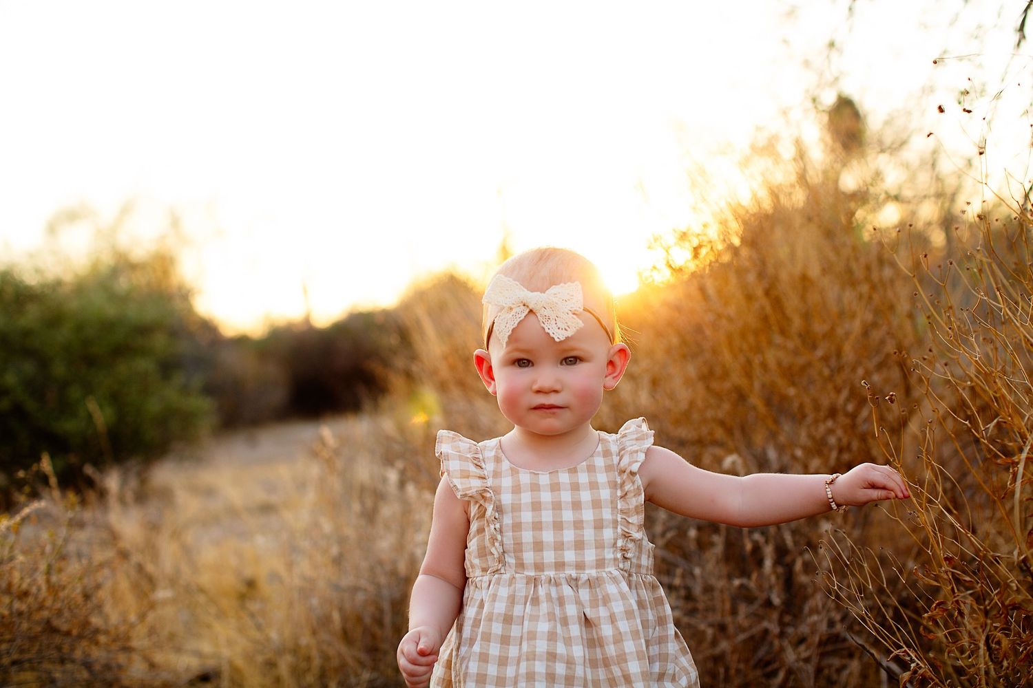 Child in a white dress playing in a golden field during sunset.