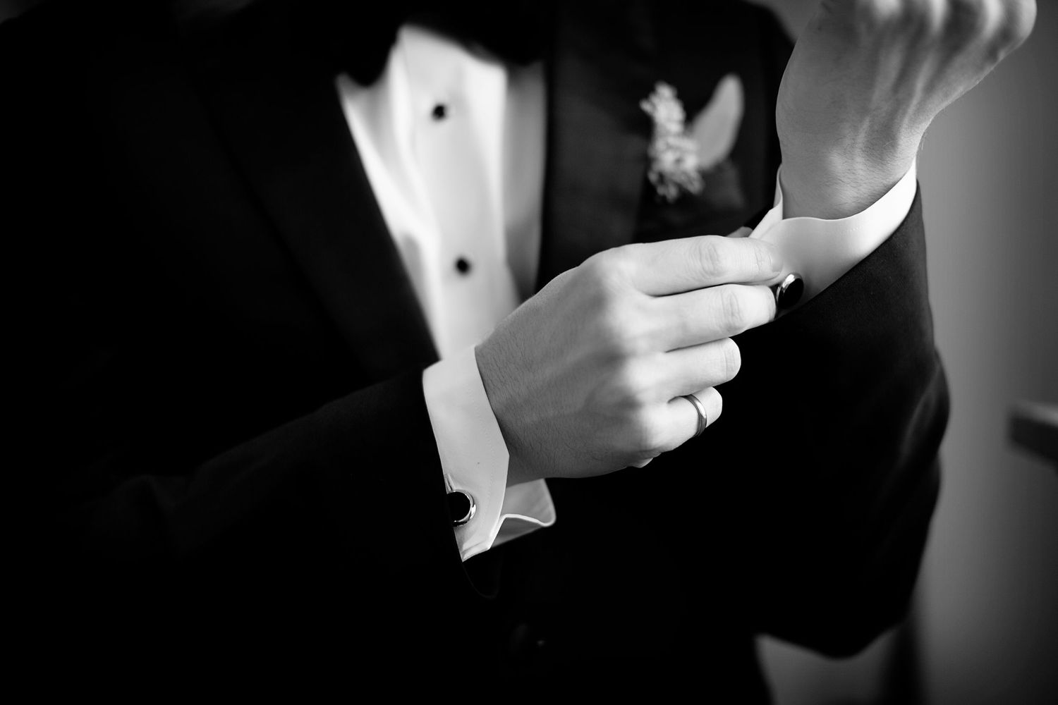 Close-up of groom adjusting tuxedo bowtie in black and white.