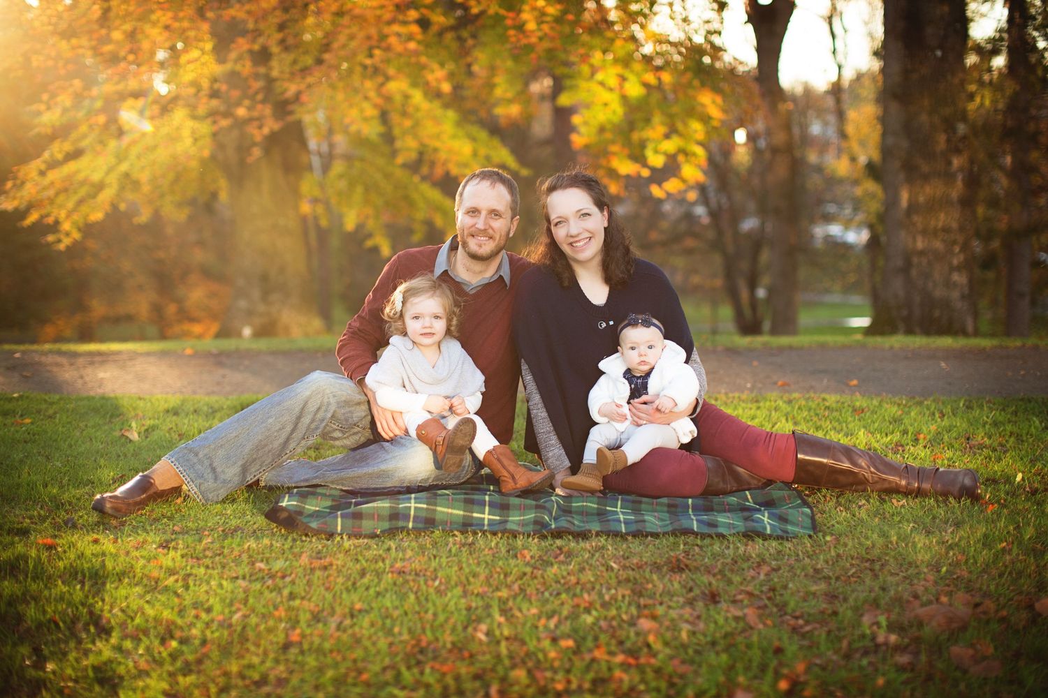 Family photo session in a park with golden autumn leaves and sunlight.
