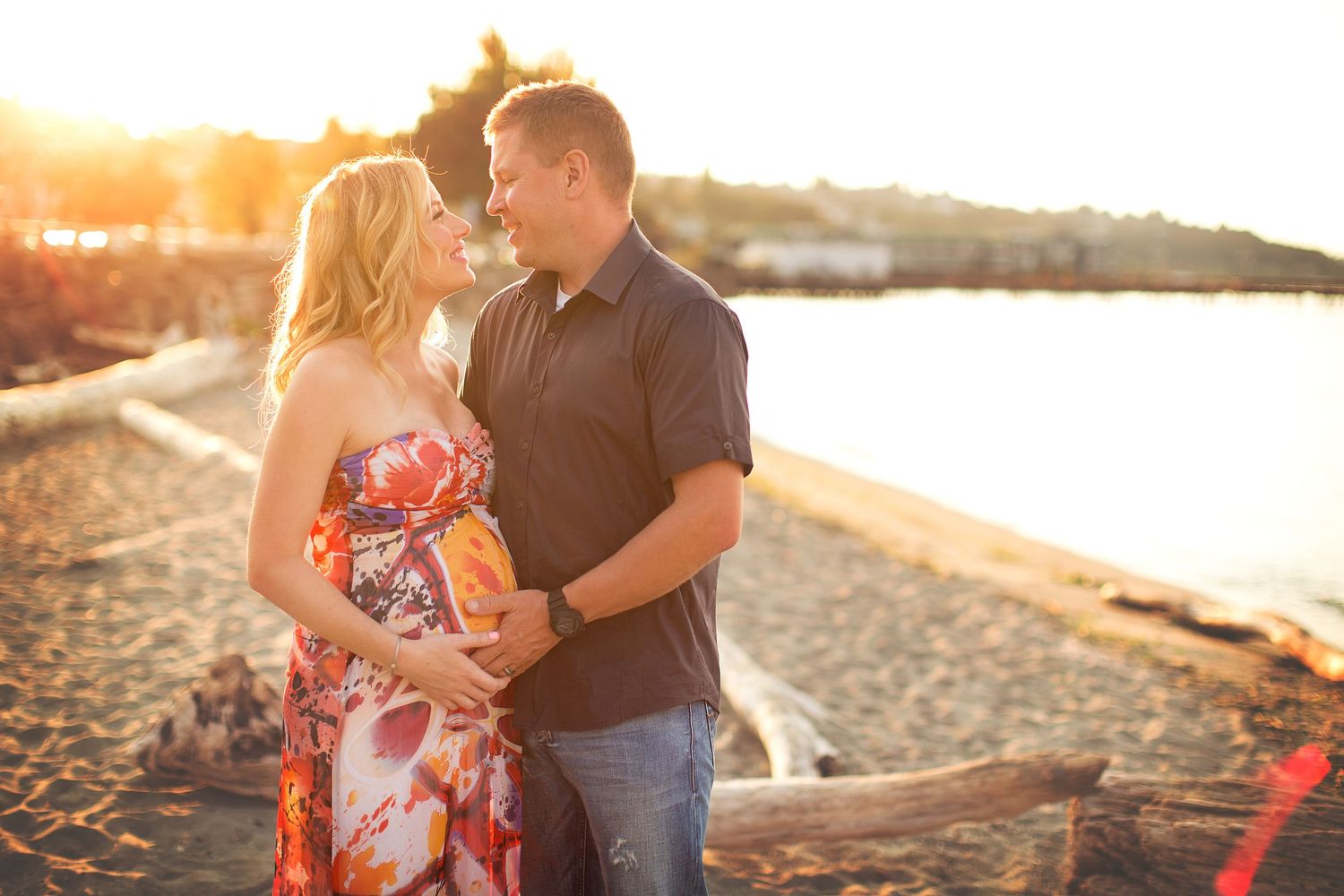 A couple embraces on a beach at sunset with golden light filtering through the trees.
