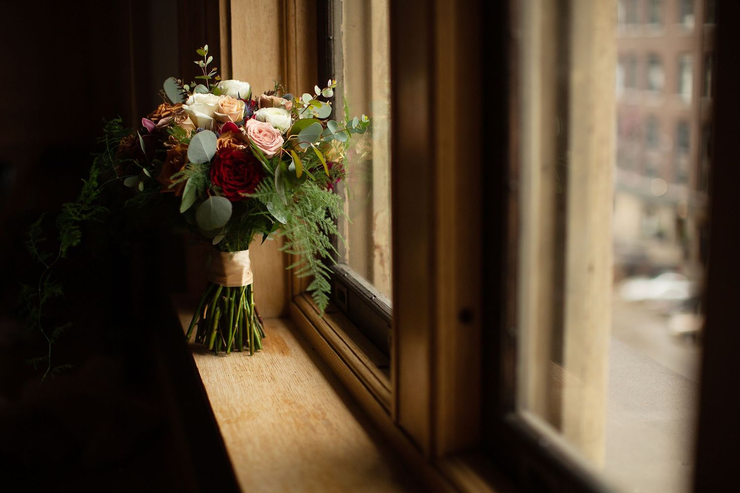 Wedding bouquet with roses sits on windowsill in natural light.