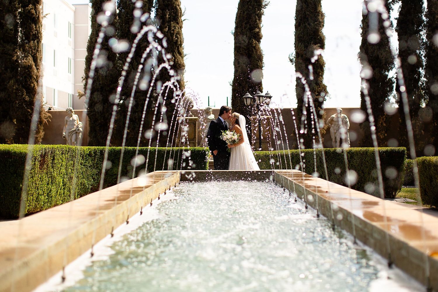 Elegant archway with stone pillars and cypress trees creates a romantic garden setting.