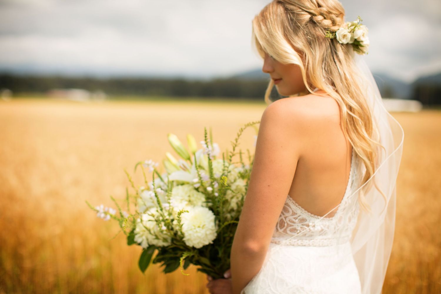 Bride holding a white and green floral bouquet against a natural outdoor backdrop.