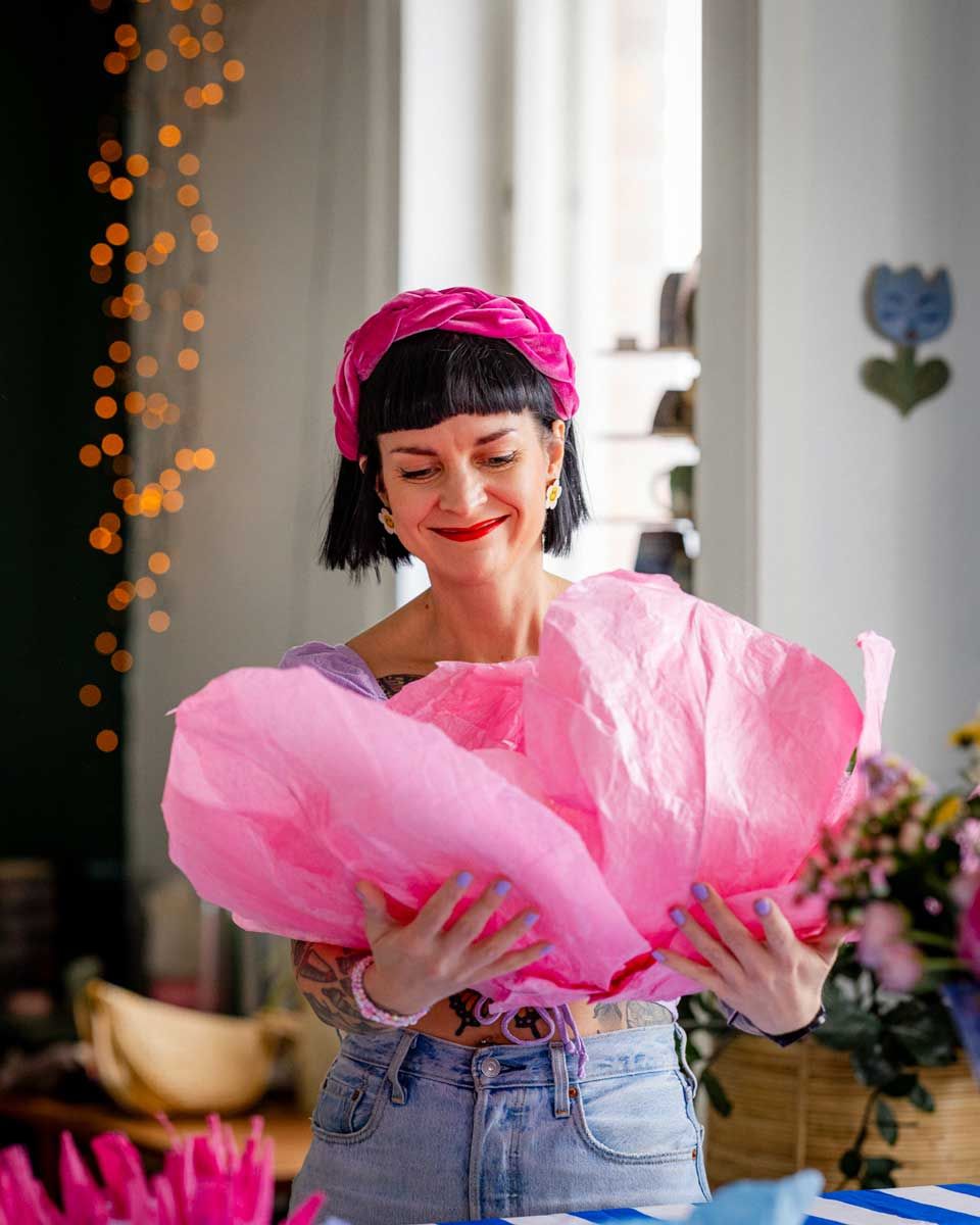 Outi Vihlman Klondyketalolla Keravalla pitämässä kukkatyöpajaa asiakkaille. Outilla on sylissä iso pinkki silkkikukka mitä hän katsoo.