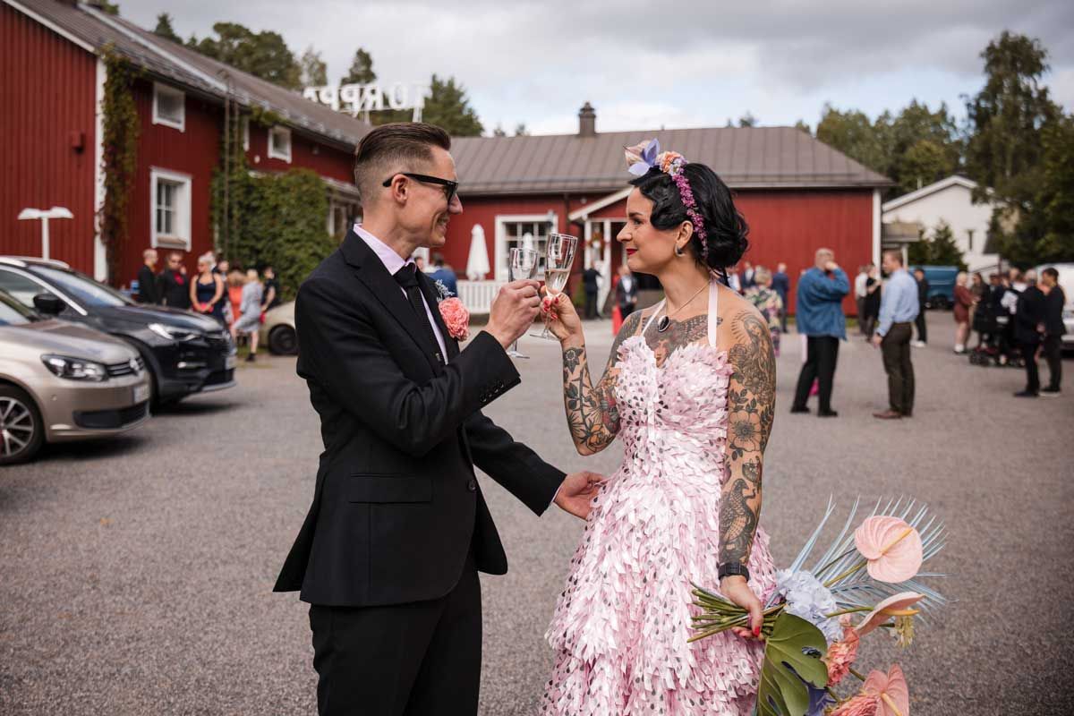 Tatuoitu morsian ja komea sulhanen kilistelee skumppalaseja Hyrylän Torpan pihalla Tuusulassa. Morsiammella on pinkku hääpuku.