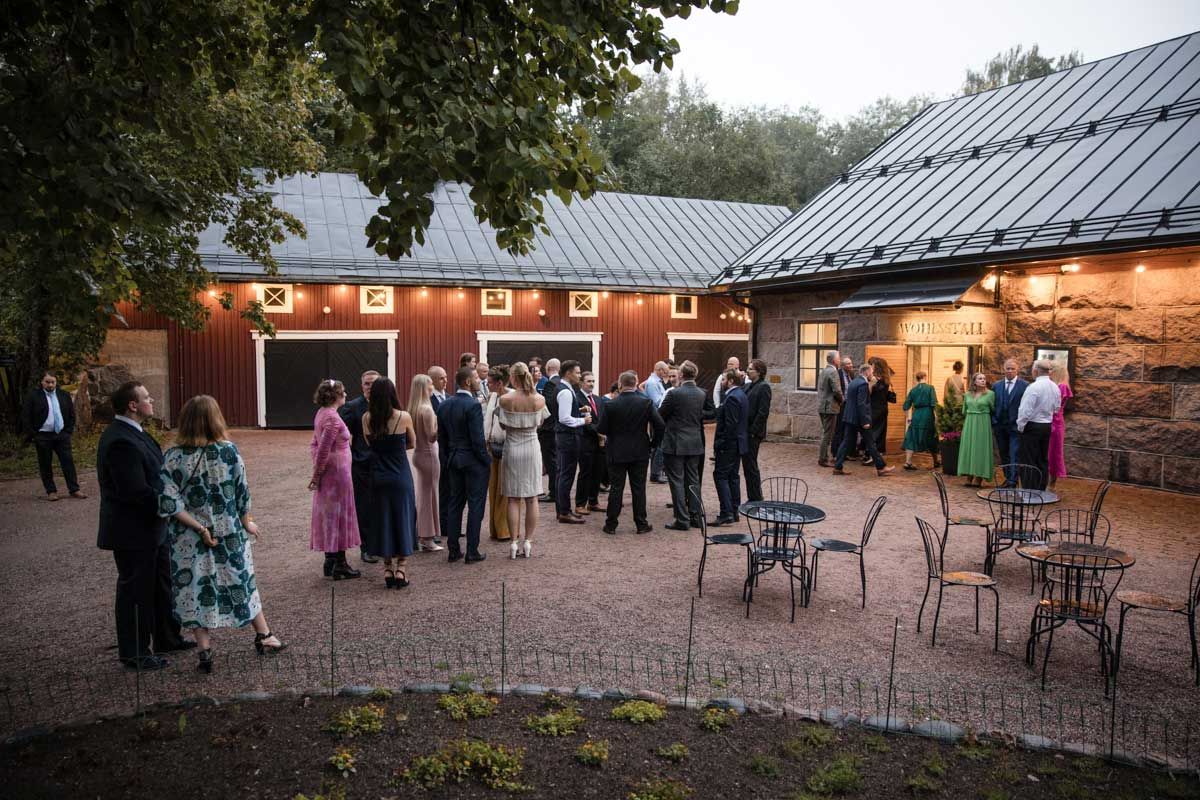 Häävieraat seisoskelee Wohls Gård juhlatilan pihalla iltahämärässä Kirkkonummella.