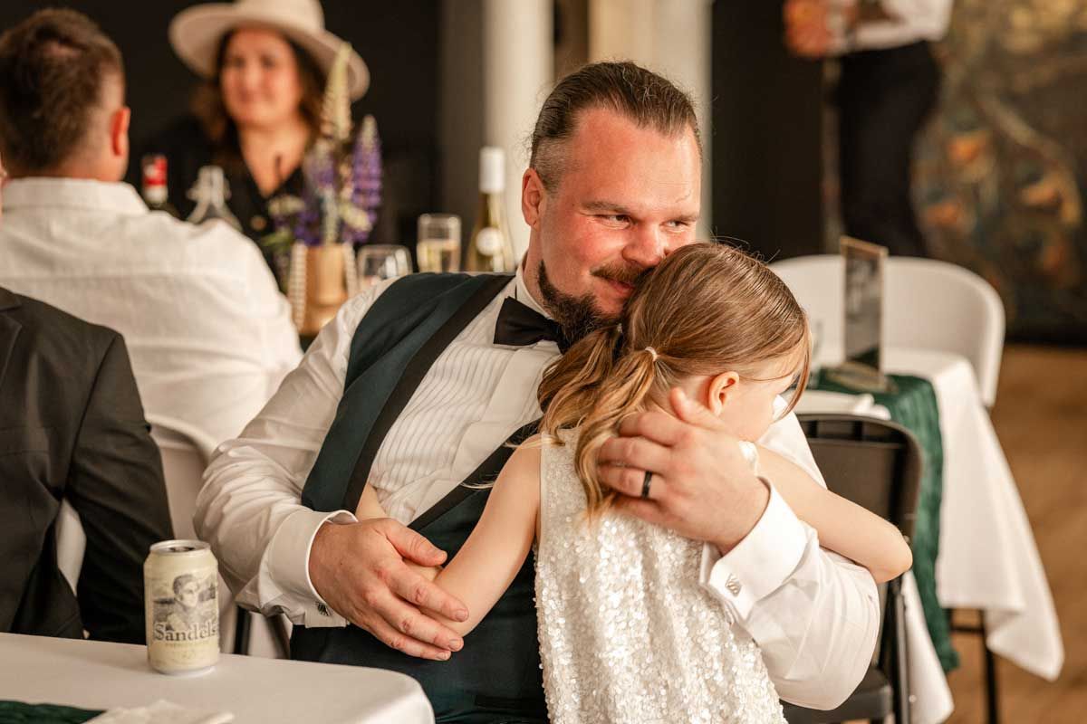 Sulhanen istuu pöydän ääressä ja halaa lämpimästi tytärtään joka on tullut tervehtimään isäänsä.