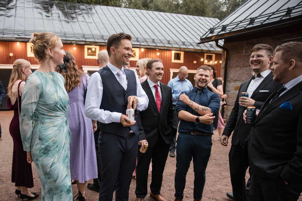 Sulhanen ja juhlavieraat seisoskelee ja juttelee iloisesti Wohls Gård juhlatilan pihalla iltahämärässä Kirkkonummella.