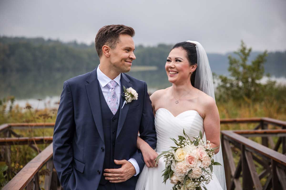 Hääpari kävelee laiturilla käsi kynkässä. Hääpari katsoo toisiaan ja hymyilee lempeästi. Taustalla järvi ja kaislikkoa. Sumuinen ilma.
