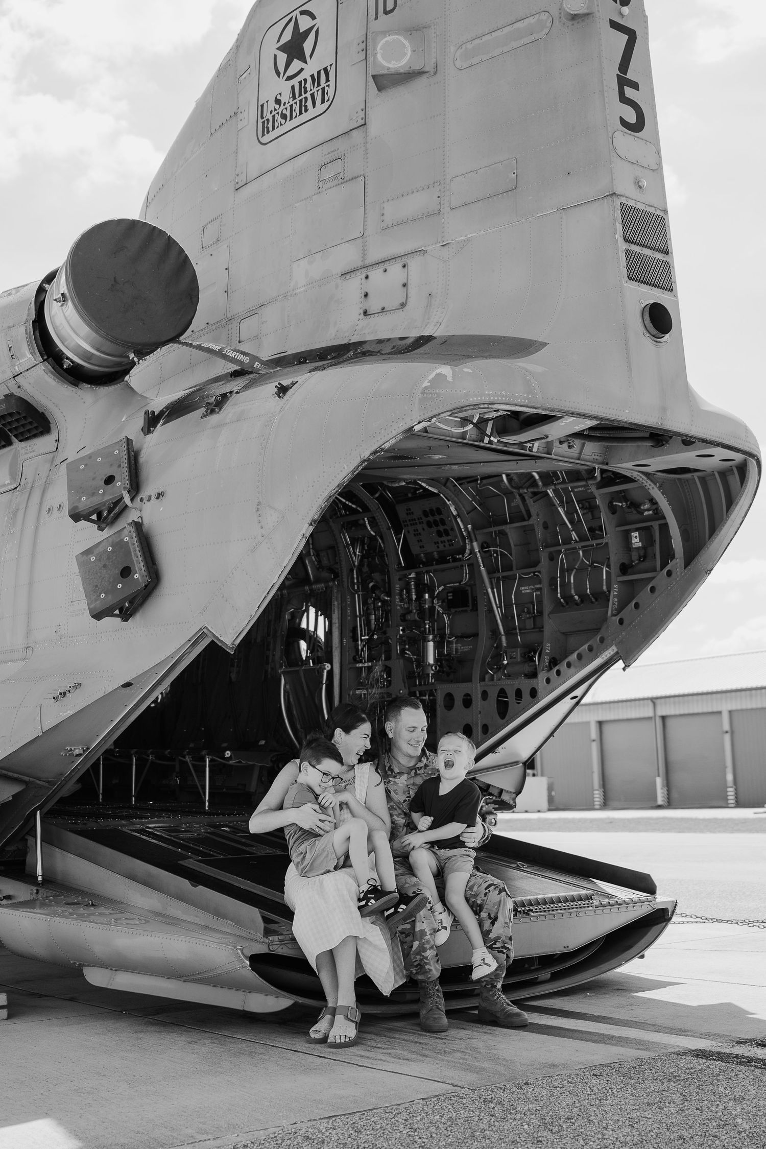 Family posing at the open rear ramp of a U.S. Army Reserve military helicopter in black and white photo.