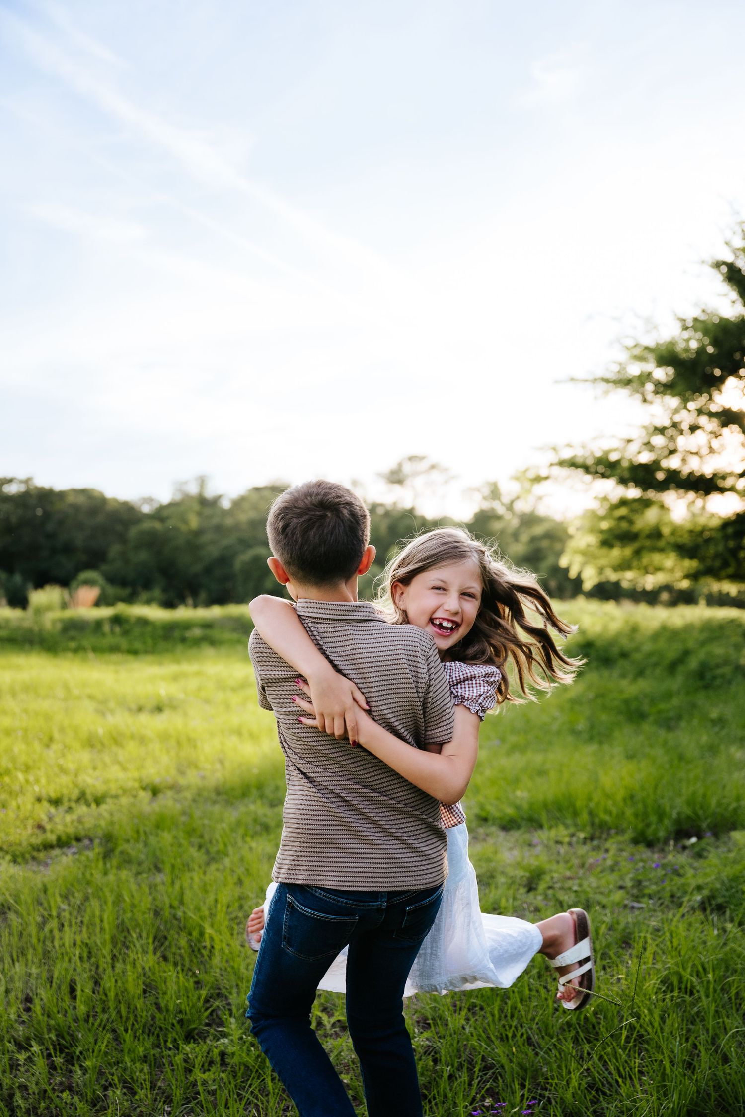 A joyful boy spinning a laughing girl in a sunny green meadow, sharing a playful and happy outdoor moment.