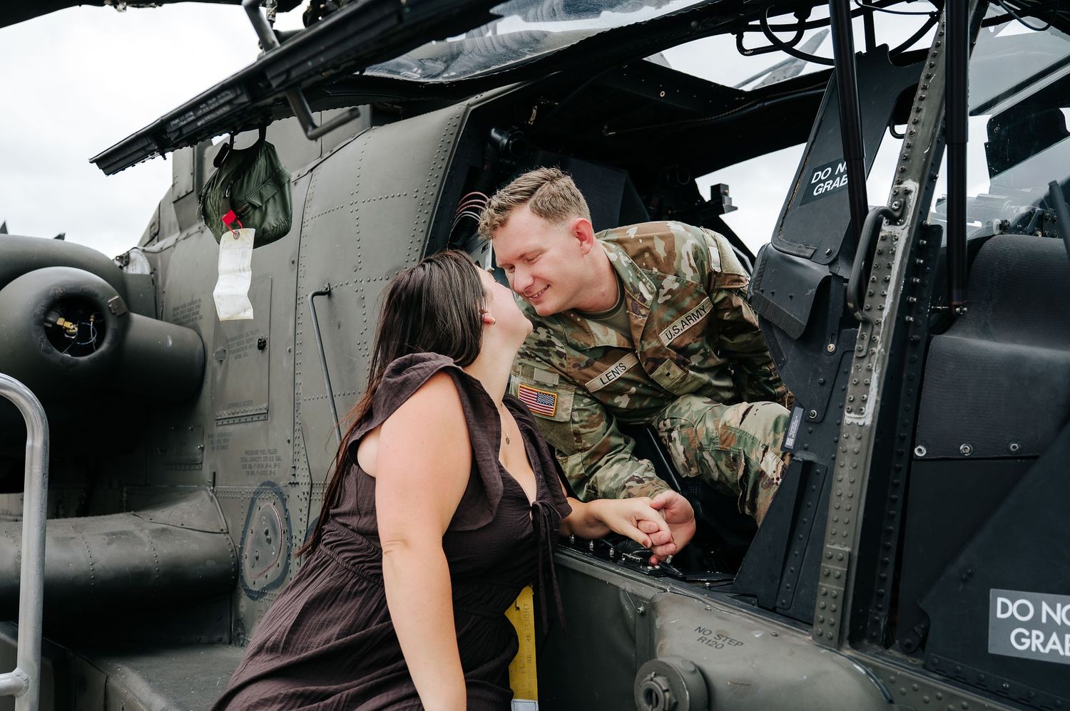 Military soldier in camouflage uniform sharing a romantic moment with a woman beside an Army helicopter.