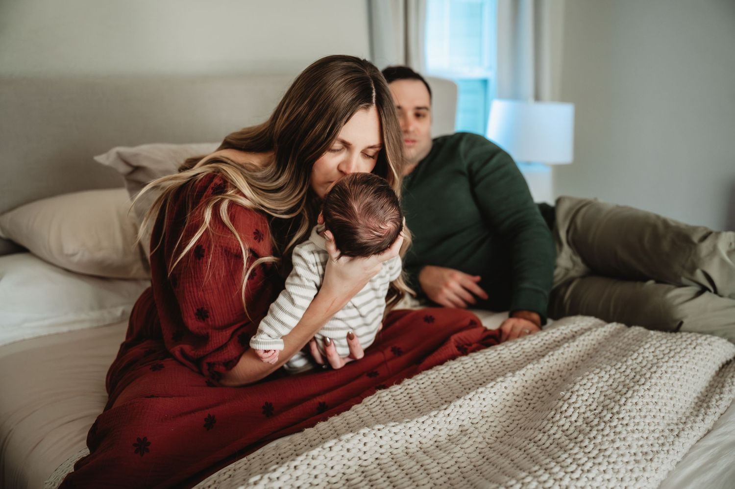 A couple cuddles together intimately on a cozy bed with white knit blankets in a romantic lifestyle setting.