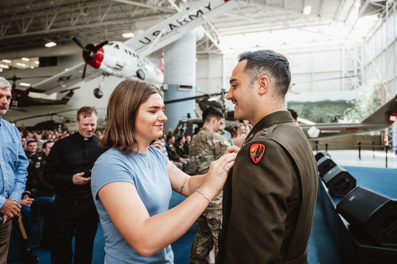 Woman pinning a badge on a U.S. Army officer's uniform at a military ceremony in an aviation museum.