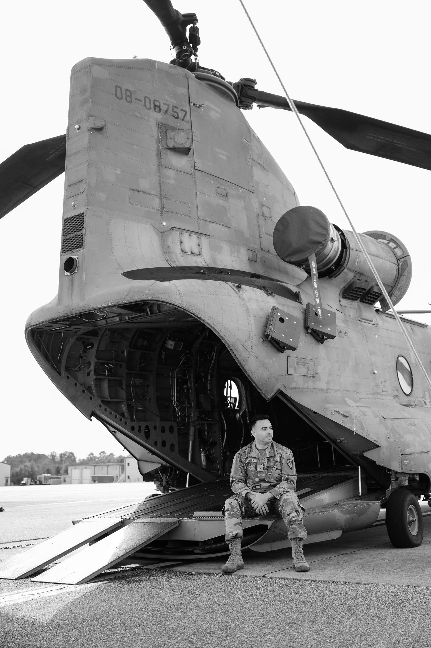 Military personnel sit beside a CH-47 Chinook helicopter on a tarmac in a black and white photo series.