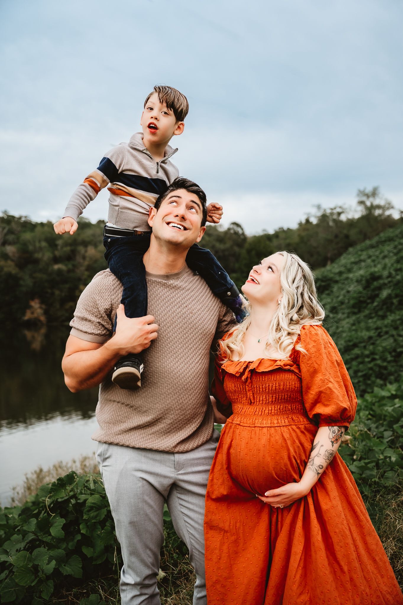 A family in coordinated outfits of orange and beige poses playfully together outdoors against green foliage.
