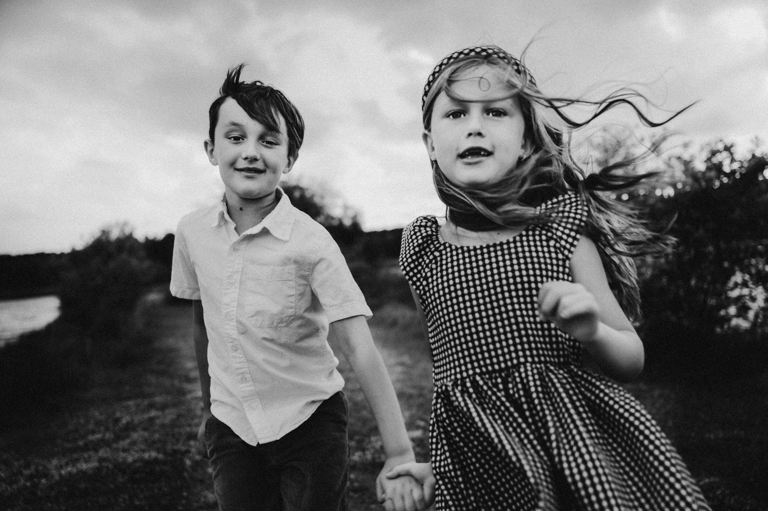 Two children run together outdoors in black and white photography.
